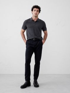 Man in a dark grey polo shirt and black pants standing in a studio