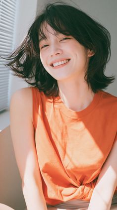 Woman with short hair and an orange top smiling in soft indoor lighting