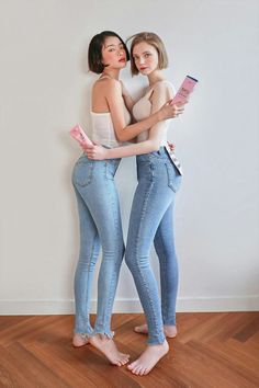 Two women in skinny jeans and tank tops holding pink products