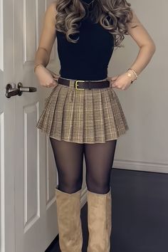 Woman in a plaid skirt, black top, and knee-high boots indoors