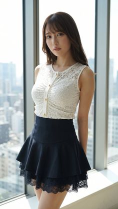 Woman in a white lace top and black skirt standing by a window with a cityscape view