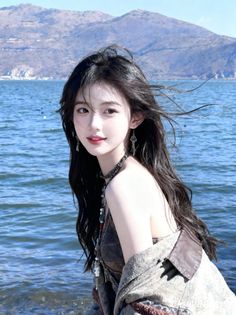 Woman with long black hair and jewelry by a lake with mountains in the background