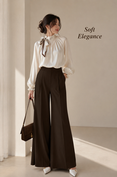 Woman in a white blouse and wide leg pants holding a brown handbag