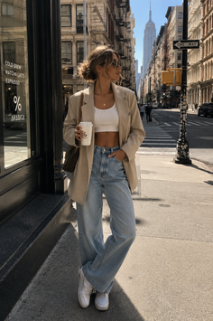 Woman in a blazer and jeans holding a coffee cup on a city street