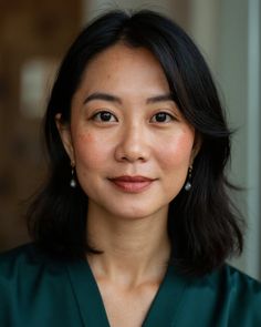 Woman with short black hair and pearl earrings in a green top
