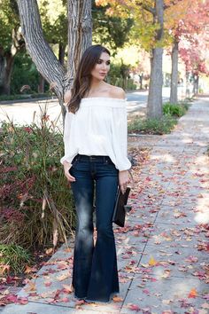 Woman in an off-shoulder top and flared jeans on a sidewalk with autumn leaves