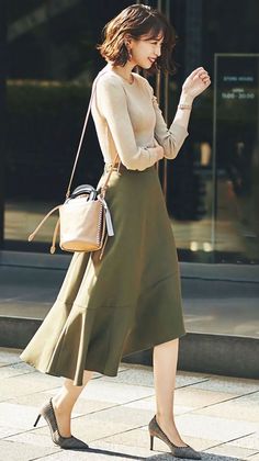 Woman with short hair in an olive skirt and long sleeve top walking outdoors