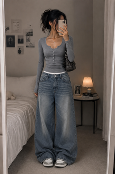 Woman in a gray long sleeve shirt and baggy jeans taking a mirror selfie