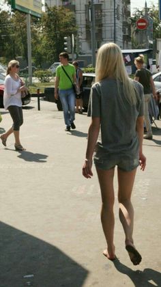 Blonde woman in denim shorts walking barefoot on a street with other people