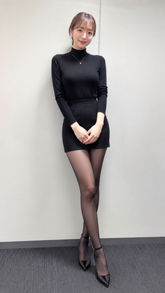 Woman in a black turtleneck, mini skirt, and tights posing indoors
