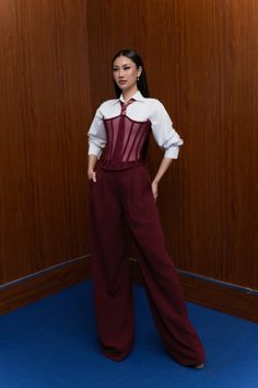 Woman in a white shirt, red corset, and wide leg pants posing indoors