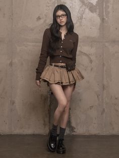 Woman with long hair and glasses wearing a brown cardigan and mini skirt