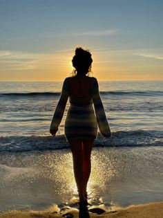 Woman in a long sleeve dress walking on a beach at sunset