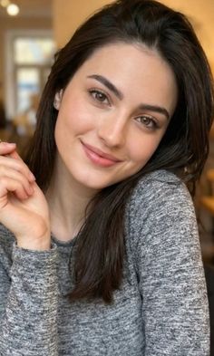 Woman with long dark hair and brown eyes wearing a gray sweater indoors