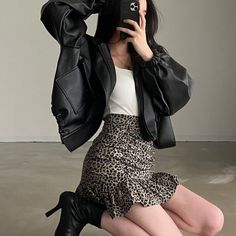 Woman in a black leather jacket and leopard print skirt taking a mirror selfie