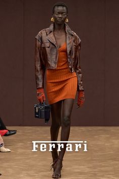 Model in a brown leather jacket and orange mini dress on a runway