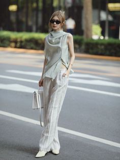 Woman in a sleeveless top and striped pants with a white handbag on a street