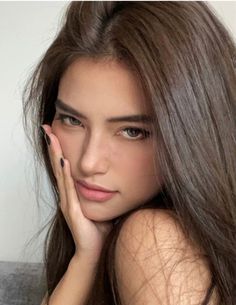 Woman with long brown hair and black nails touching her face