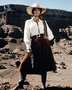 Woman in a cowgirl hat and western wear holding a revolver in a desert landscape