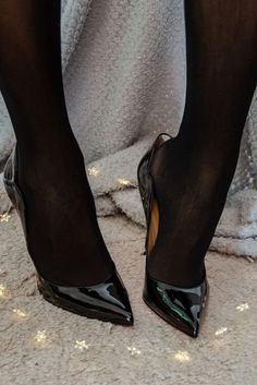 Legs in black tights and patent leather high heels on a textured surface
