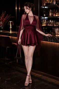Woman in a burgundy dress with a sheer overlay standing at a bar