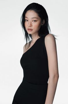 Woman with black hair wearing a black one-shoulder top in a studio