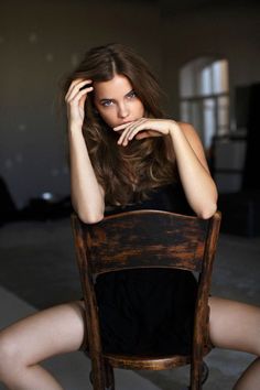 Woman with long hair and blue eyes in a black dress sitting on a wooden chair
