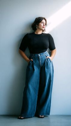 Woman with short hair wearing a black top and wide leg jeans indoors
