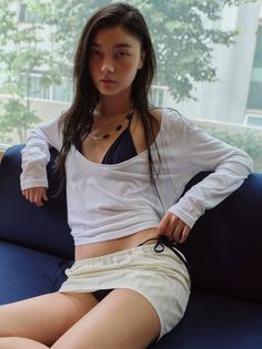 Woman in a bikini top and mini skirt sitting on a blue couch indoors