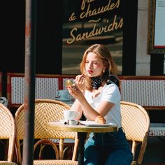 Woman with blonde hair applying lipstick at an outdoor cafe