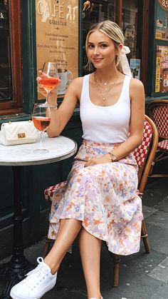Woman with blonde hair in a floral skirt and white tank top at an outdoor cafe