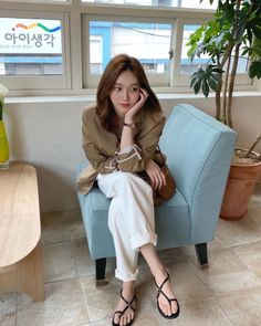 Woman with brown hair wearing a blazer and white pants, sitting indoors