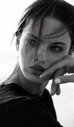 Black and white portrait of a woman with freckles and long hair, resting her chin on her hand