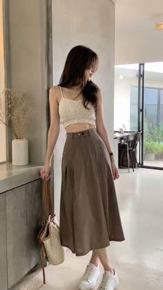 Woman in a crochet top and midi skirt holding a straw bag indoors