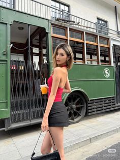 Woman in a red halter top and black mini skirt posing next to a green tram