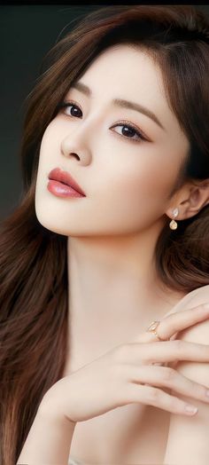 Woman with long brown hair, wearing earrings and a ring, with soft lighting