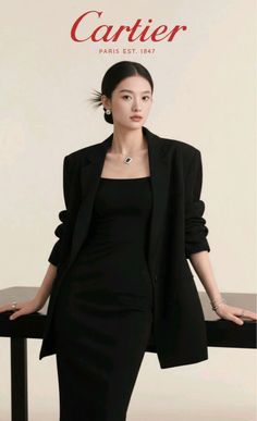 Woman in a black dress and blazer with an updo and jewelry in a studio