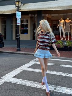 Woman with long blonde hair wearing a striped shirt and pleated mini skirt on a street