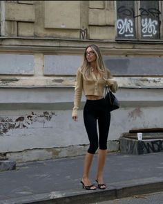 Woman with long hair and glasses wearing a cropped cardigan and capris on a street