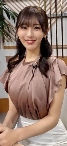 Woman with brown hair and bangs wearing a brown top with ruffle sleeves