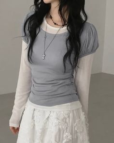 Person with long dark hair wearing layered top and white floral skirt