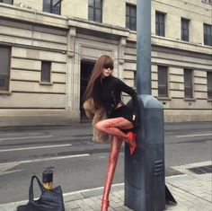 Woman in a black top, red tights, and fur coat posing on a city street