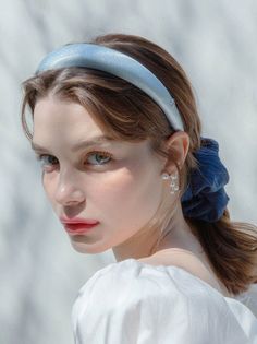 Woman with a blue headband and pearl earrings looking at the camera