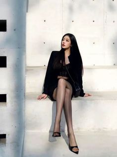 Woman with long black hair wearing a black lace top and pantyhose, sitting outdoors