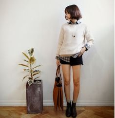 Woman in a chunky knit sweater and denim shorts holding a brown bag indoors