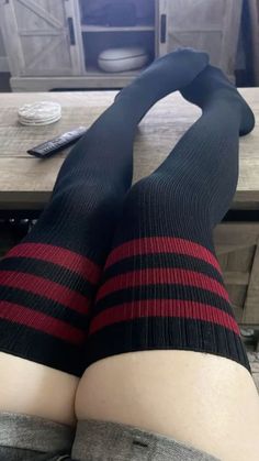 Person wearing thigh-high socks with red stripes, legs resting on a wooden table