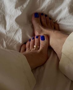 Feet with blue nail polish and a toe ring on white bedding