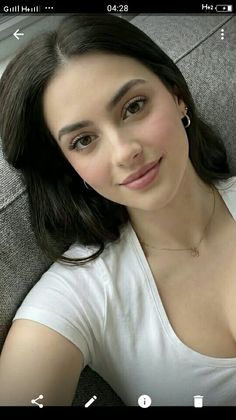 Woman with dark hair wearing a white t-shirt and gold necklace indoors