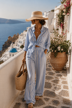 Woman in a striped outfit and straw hat walking on a path in Santorini