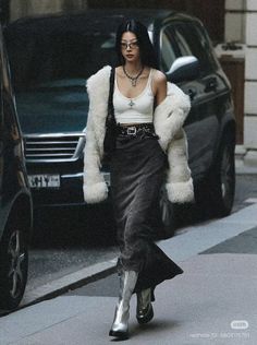 Woman in a fur coat, crop top, and long skirt walking on a street